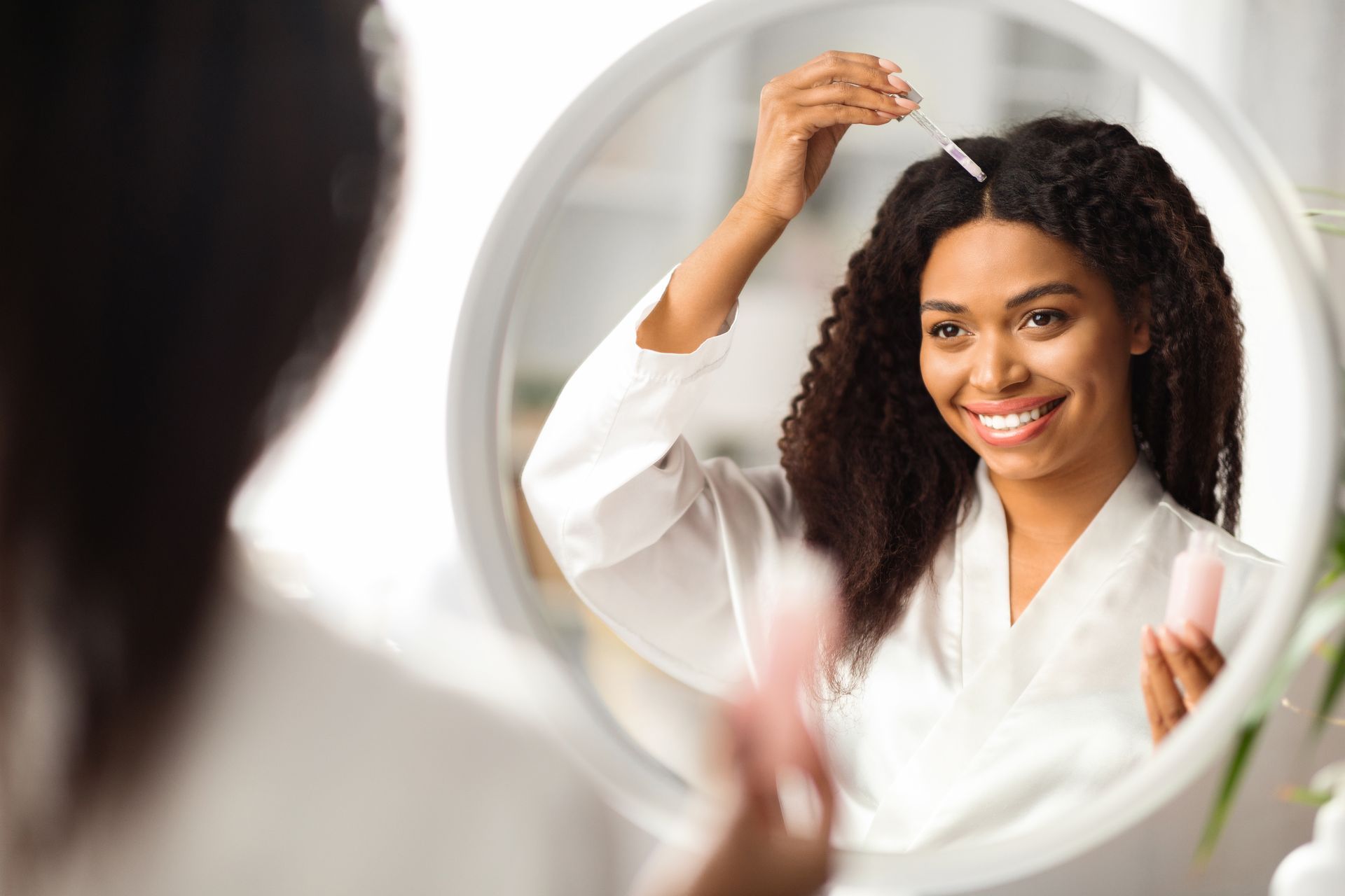 A woman is applying a serum to her hair in front of a mirror.