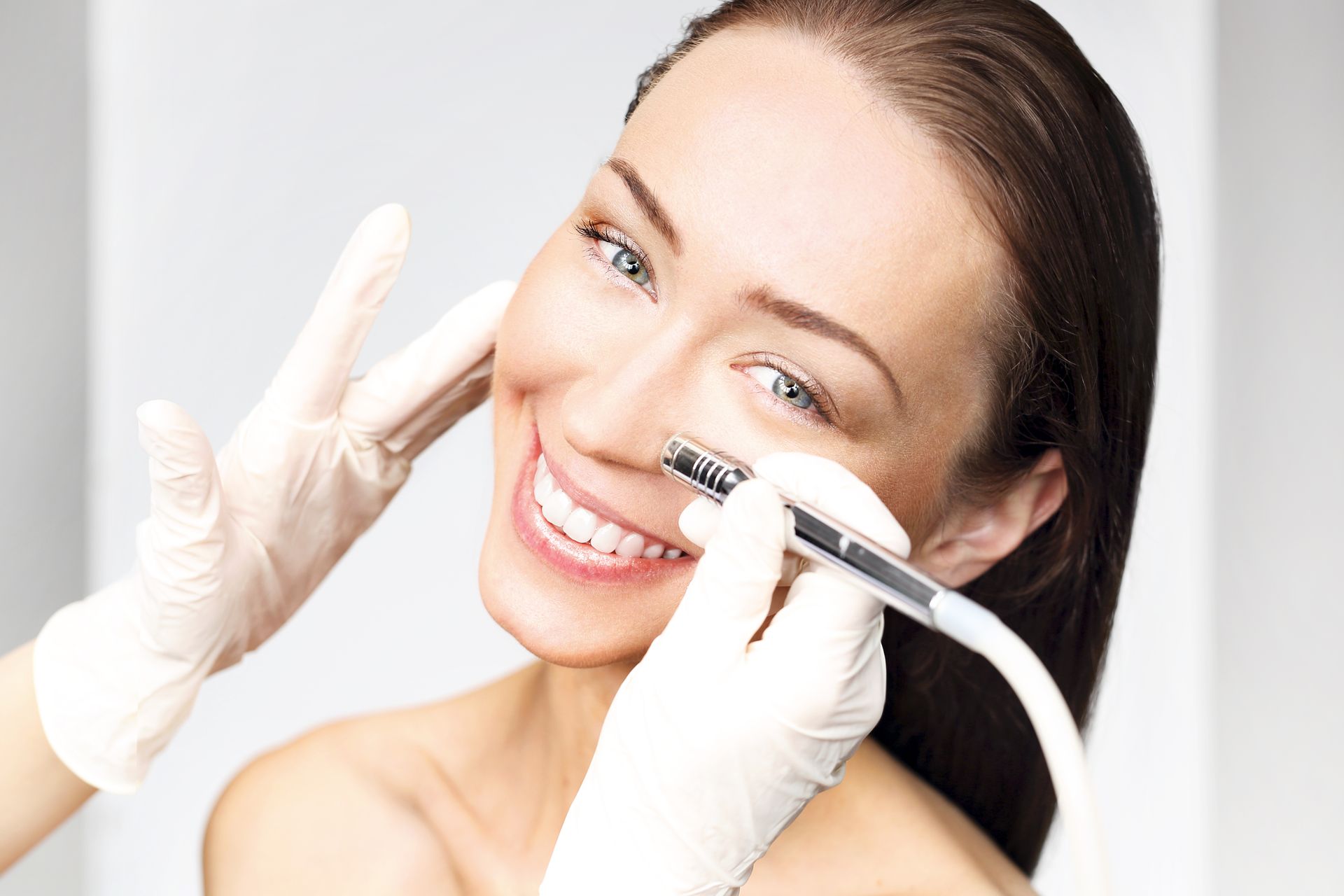 A woman is smiling while getting a treatment on her face