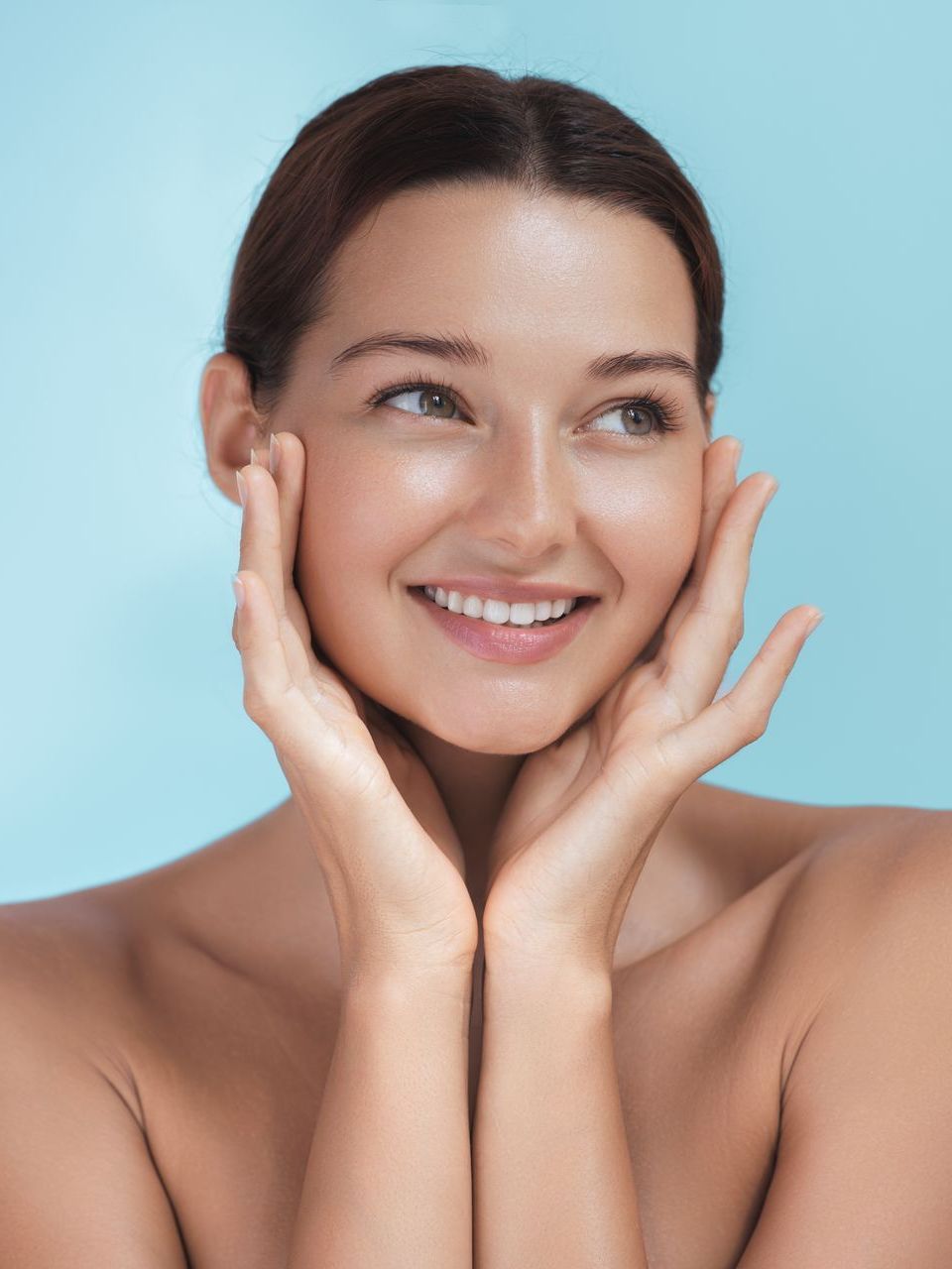 A woman is smiling and touching her face with her hands.