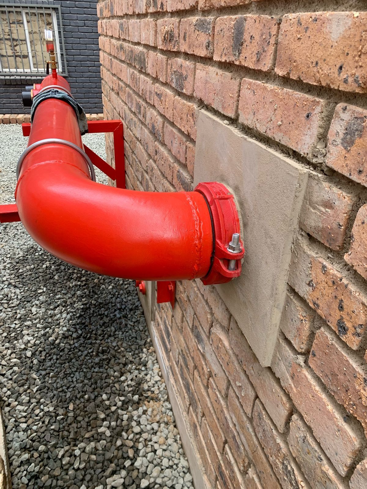 A red pipe is attached to a brick wall.