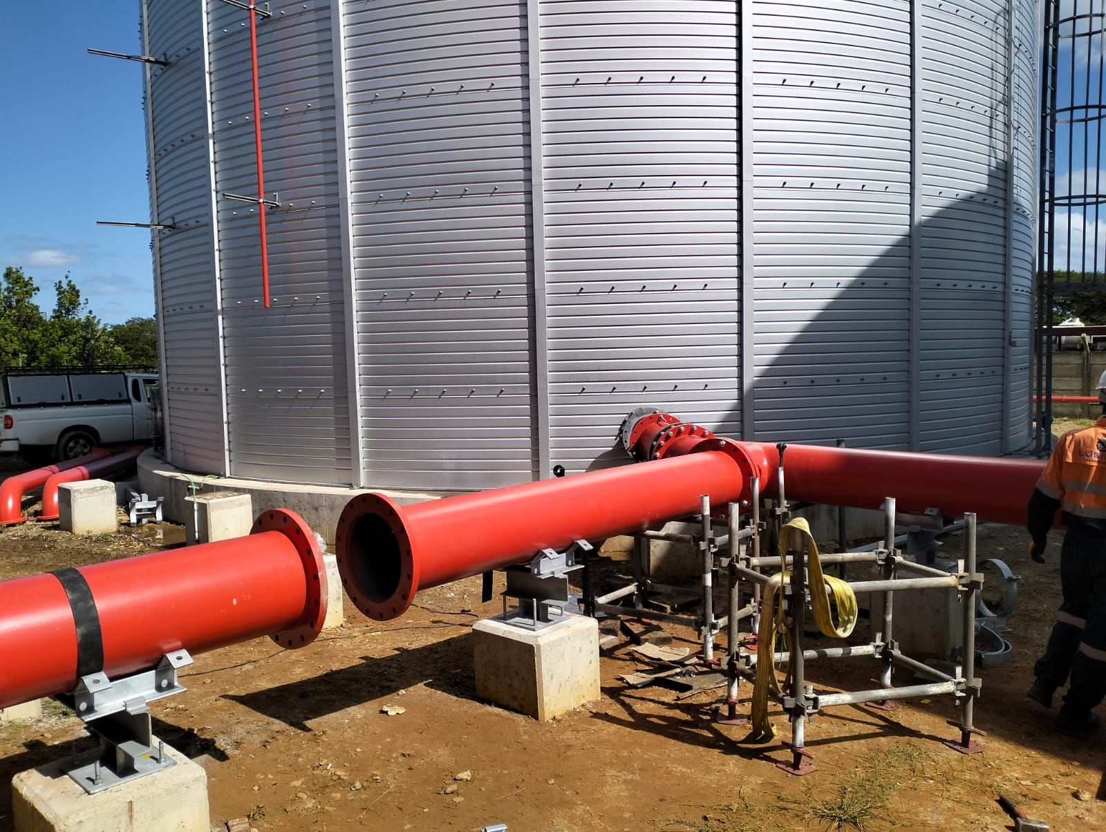 A group of red pipes are being installed in front of a silo.