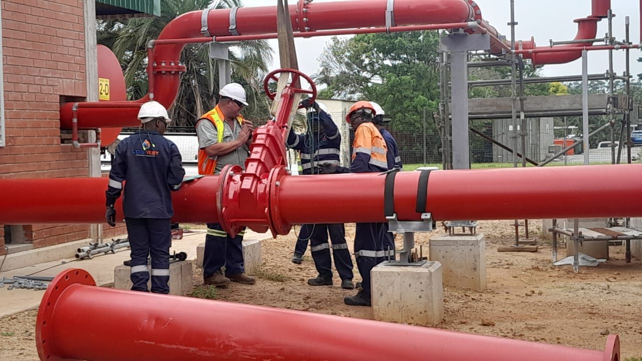 A group of men are working on a red pipe.
