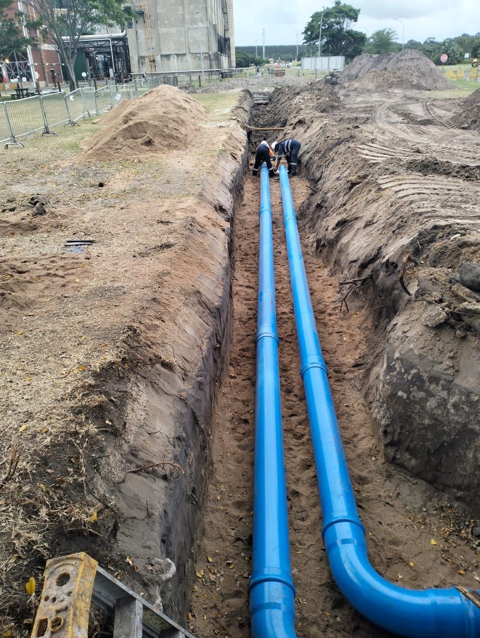 Two blue pipes are being installed in a trench.