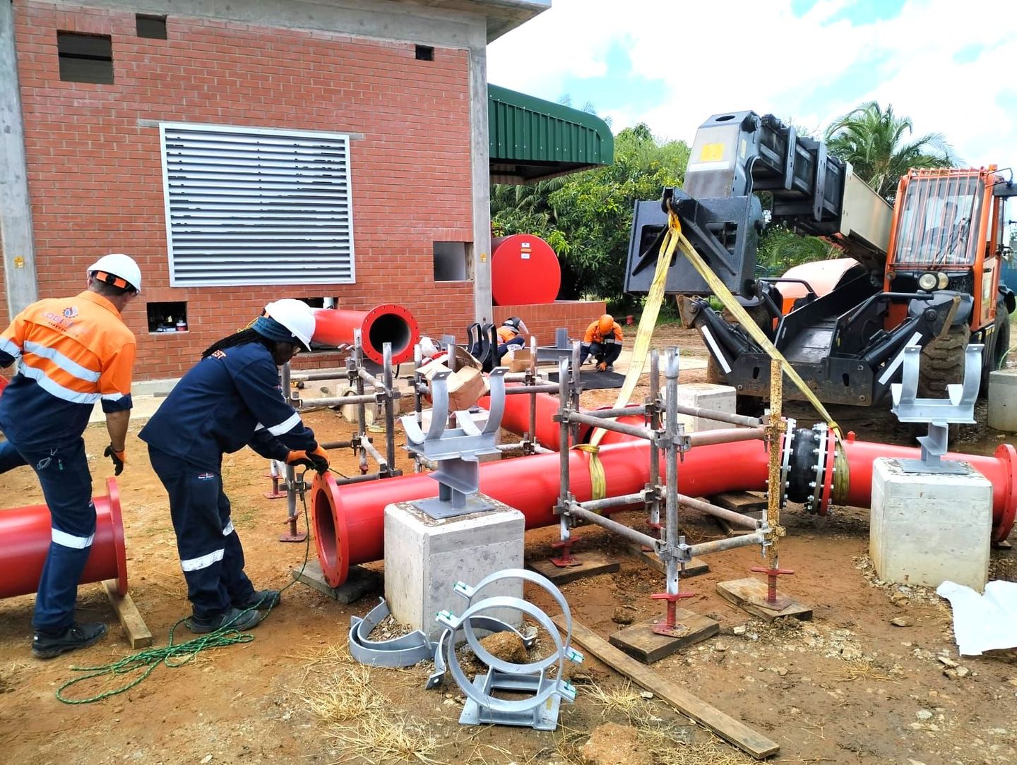 A group of construction workers are working on a large red pipe.