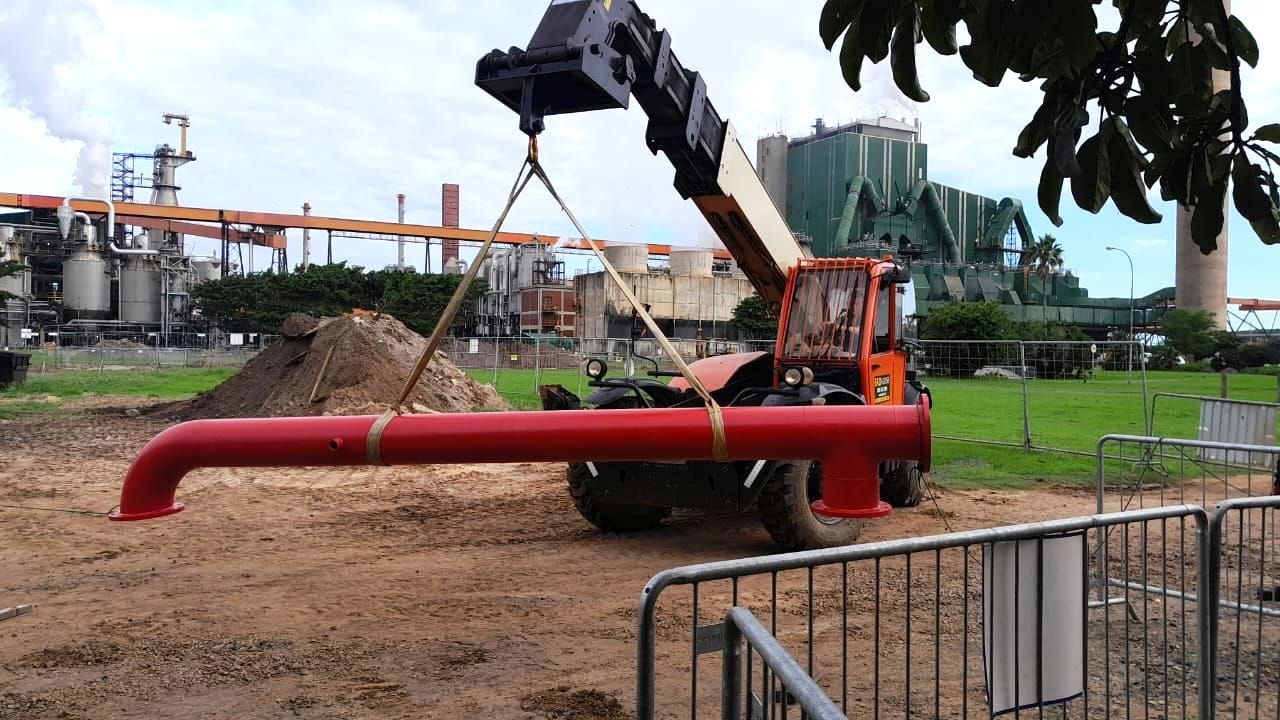 A large red pipe is being lifted by a crane.