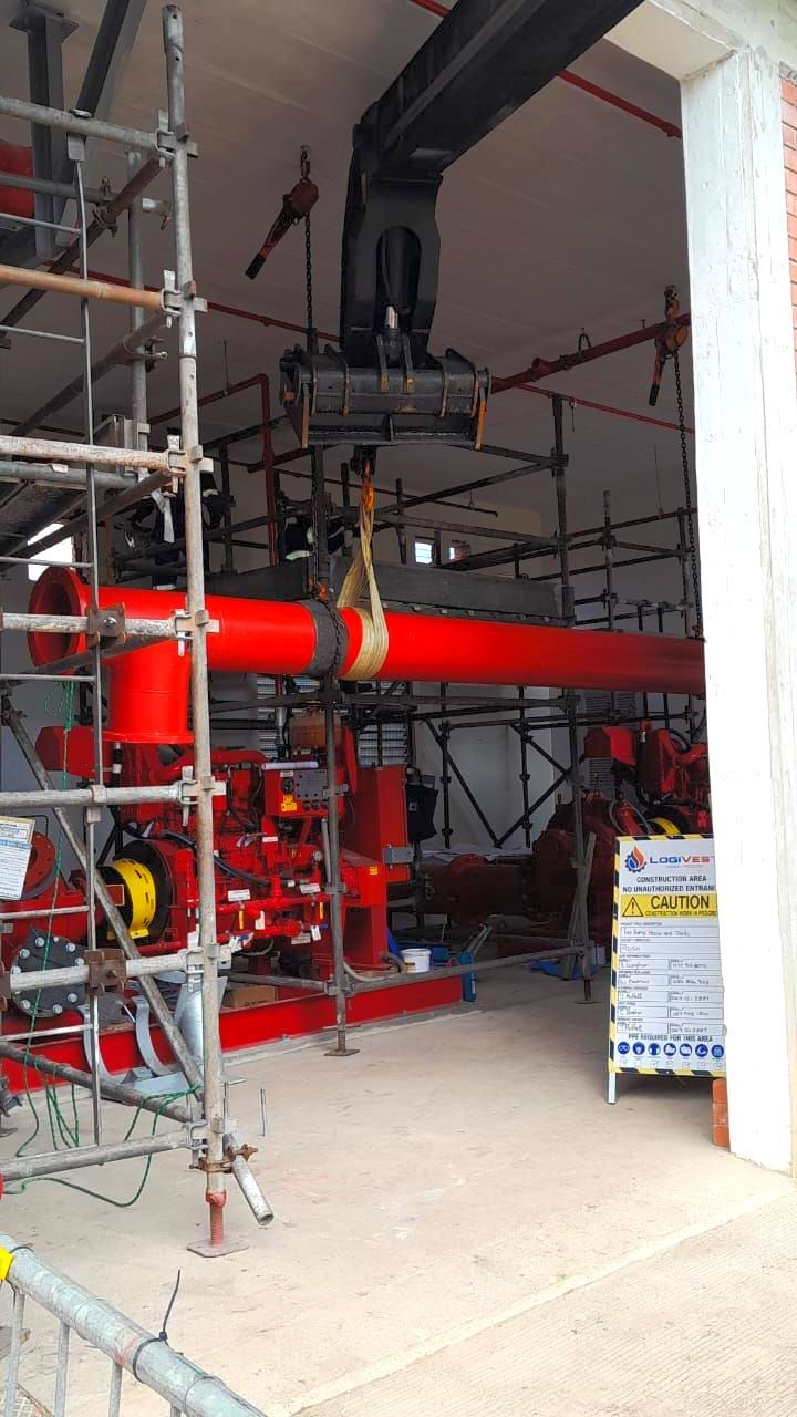 A large red pipe is being lifted by a crane in a building under construction.