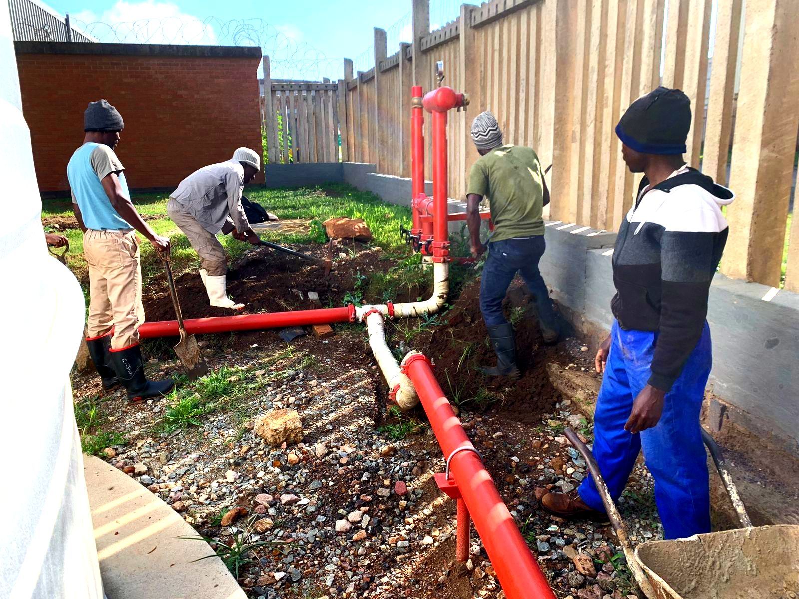 A group of men are working on a fire hydrant in the dirt.