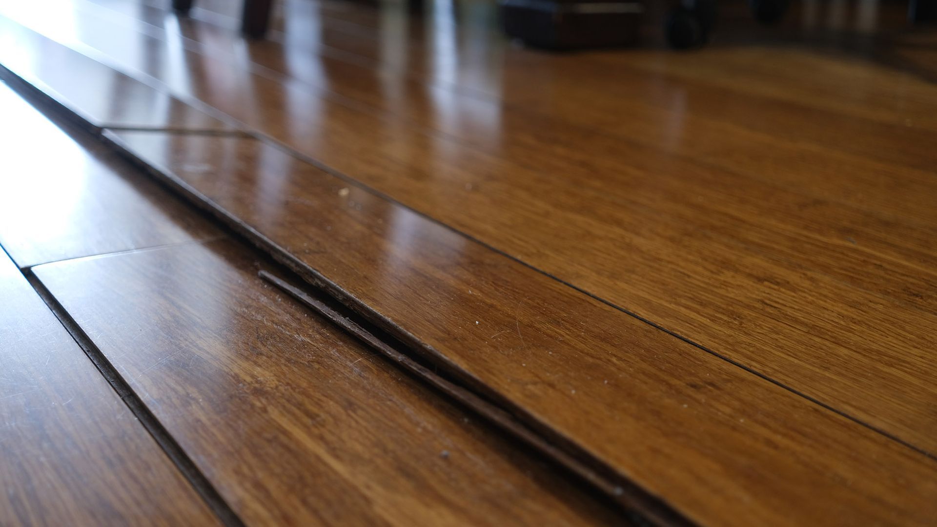Close-up of wooden floorboards with a noticeable gap between two planks, highlighting the floor's imperfections.