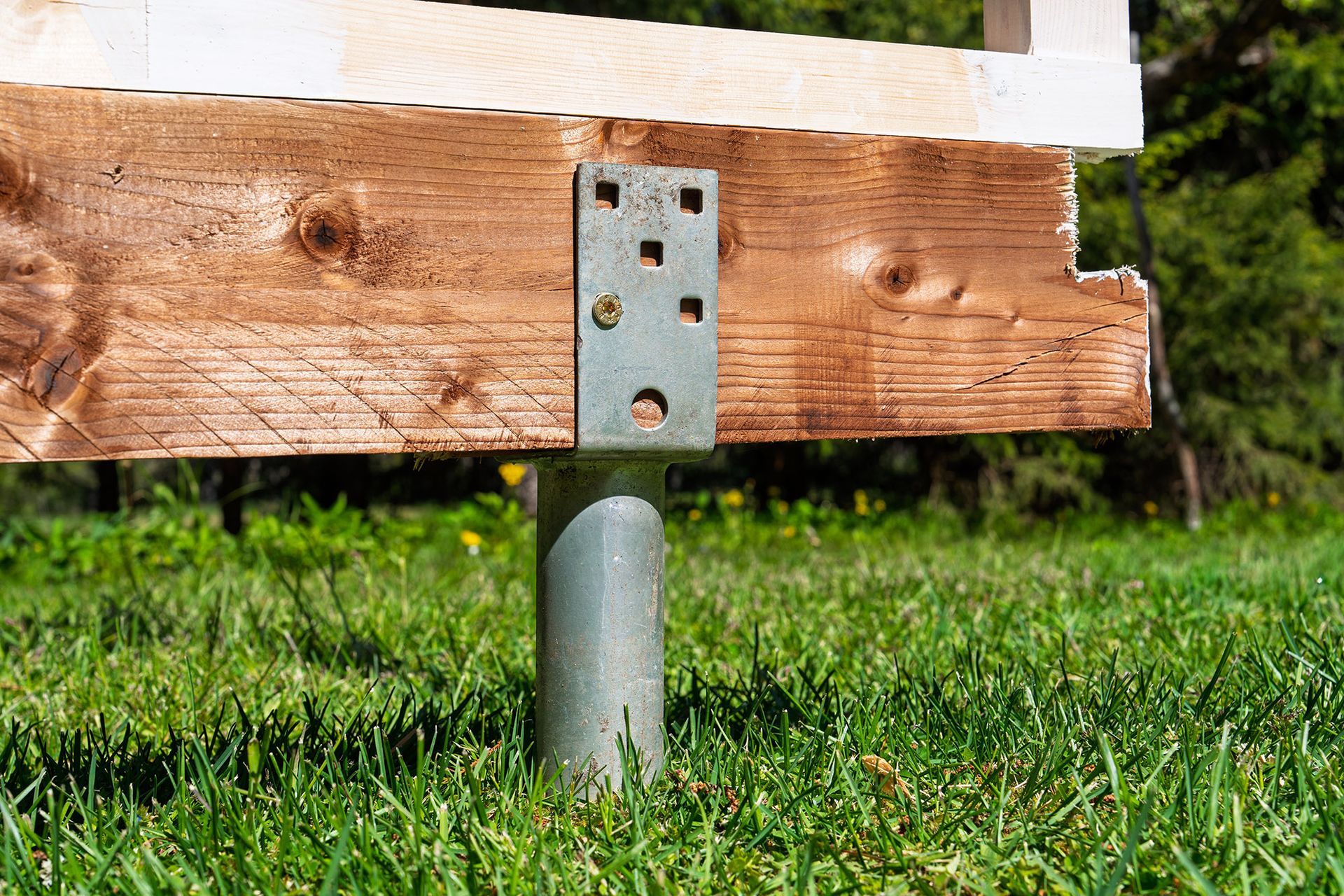 Wooden beam attached to a metal post with a bracket, set in green grass.