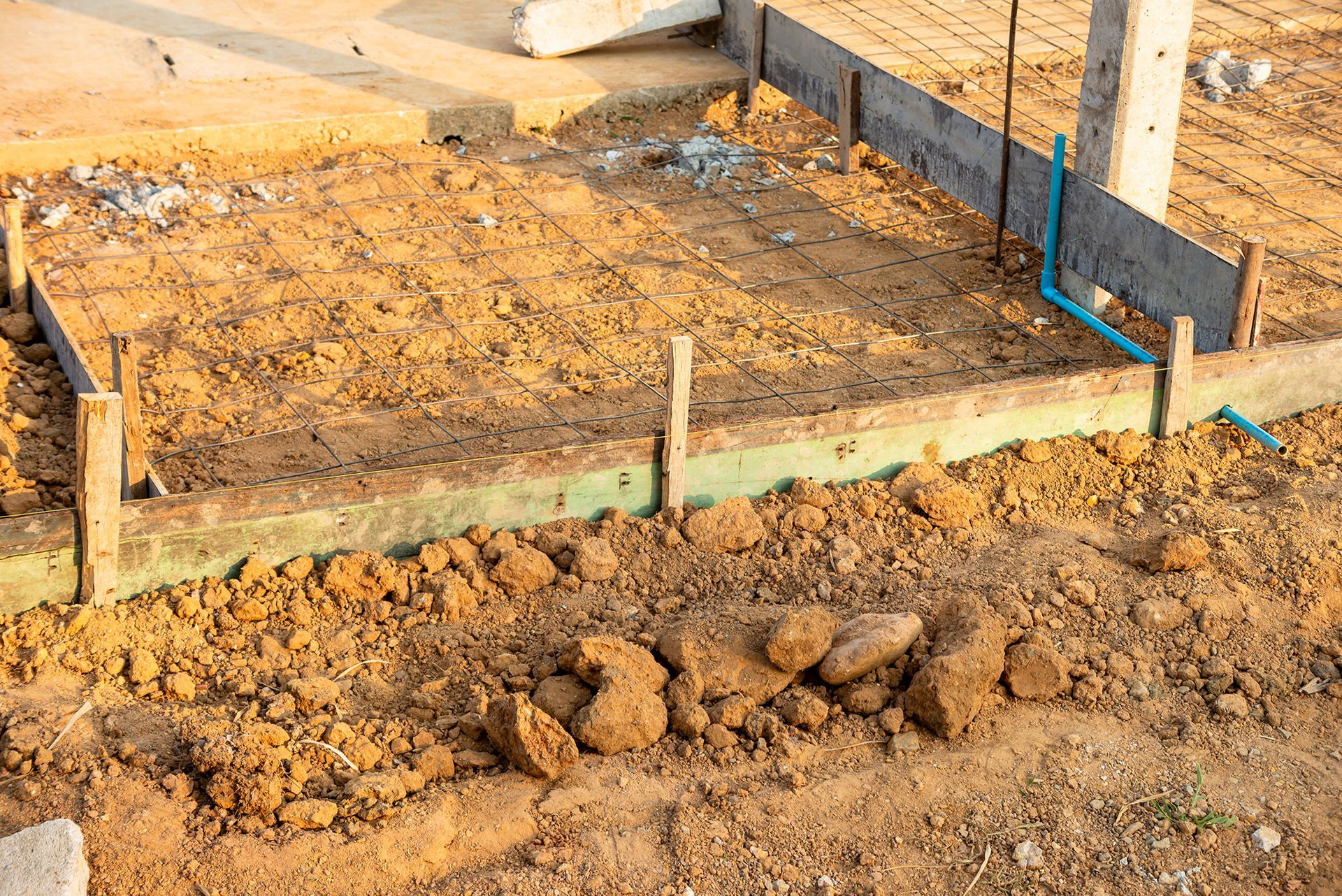 Construction site with wooden forms for concrete, exposed soil, and a blue pipe.