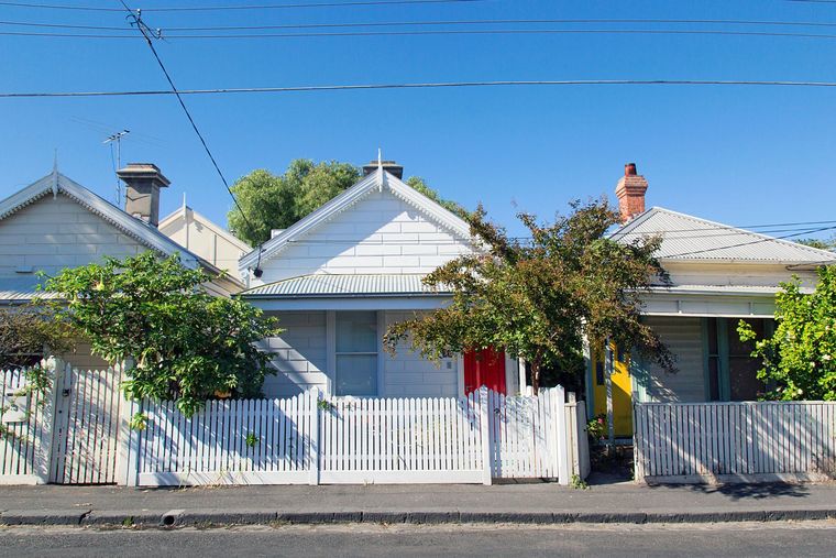 Row of white houses with picket fences, red door, and green trees against a blue sky.