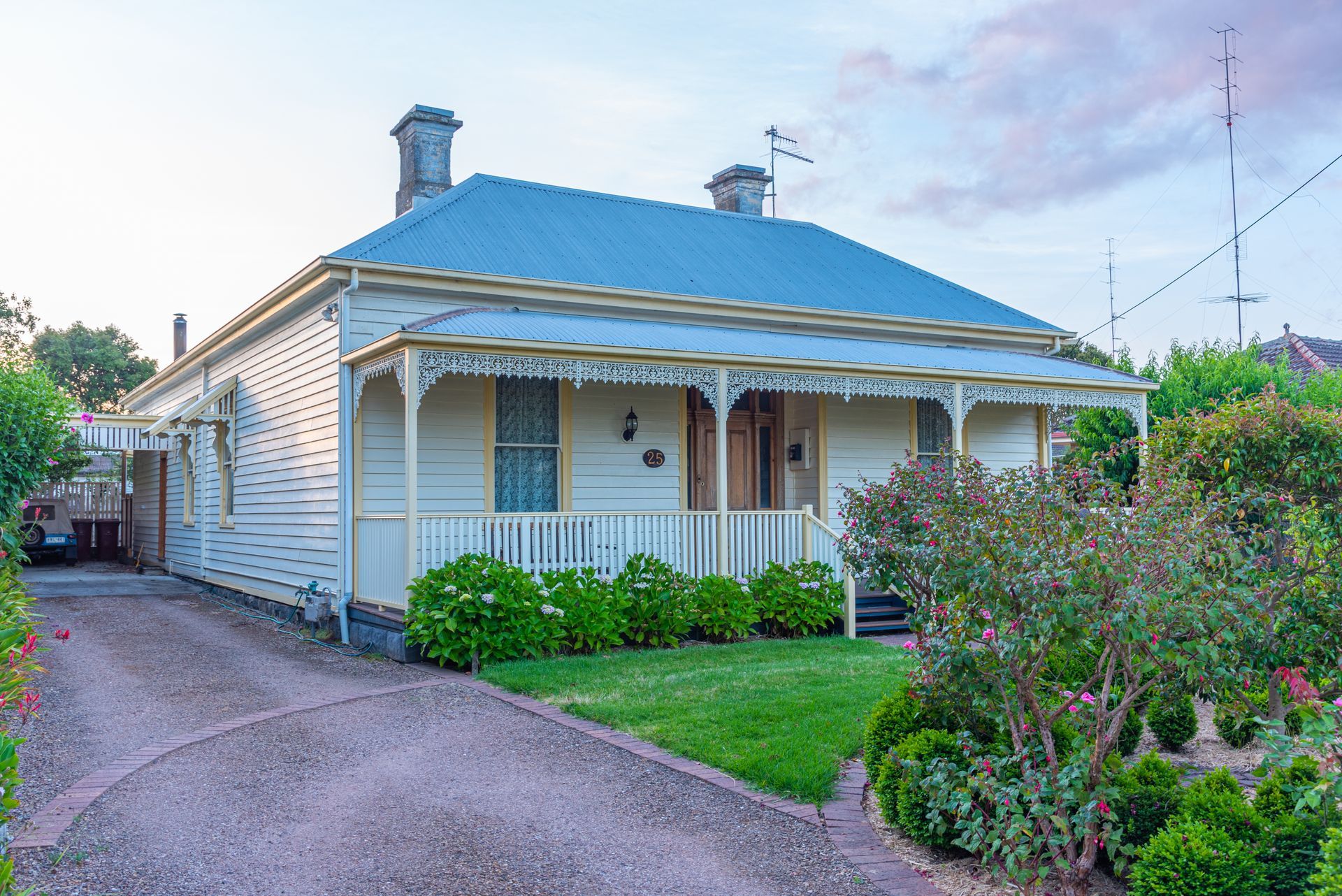 A pale yellow Victorian house with porch, green lawn, and a gray driveway.