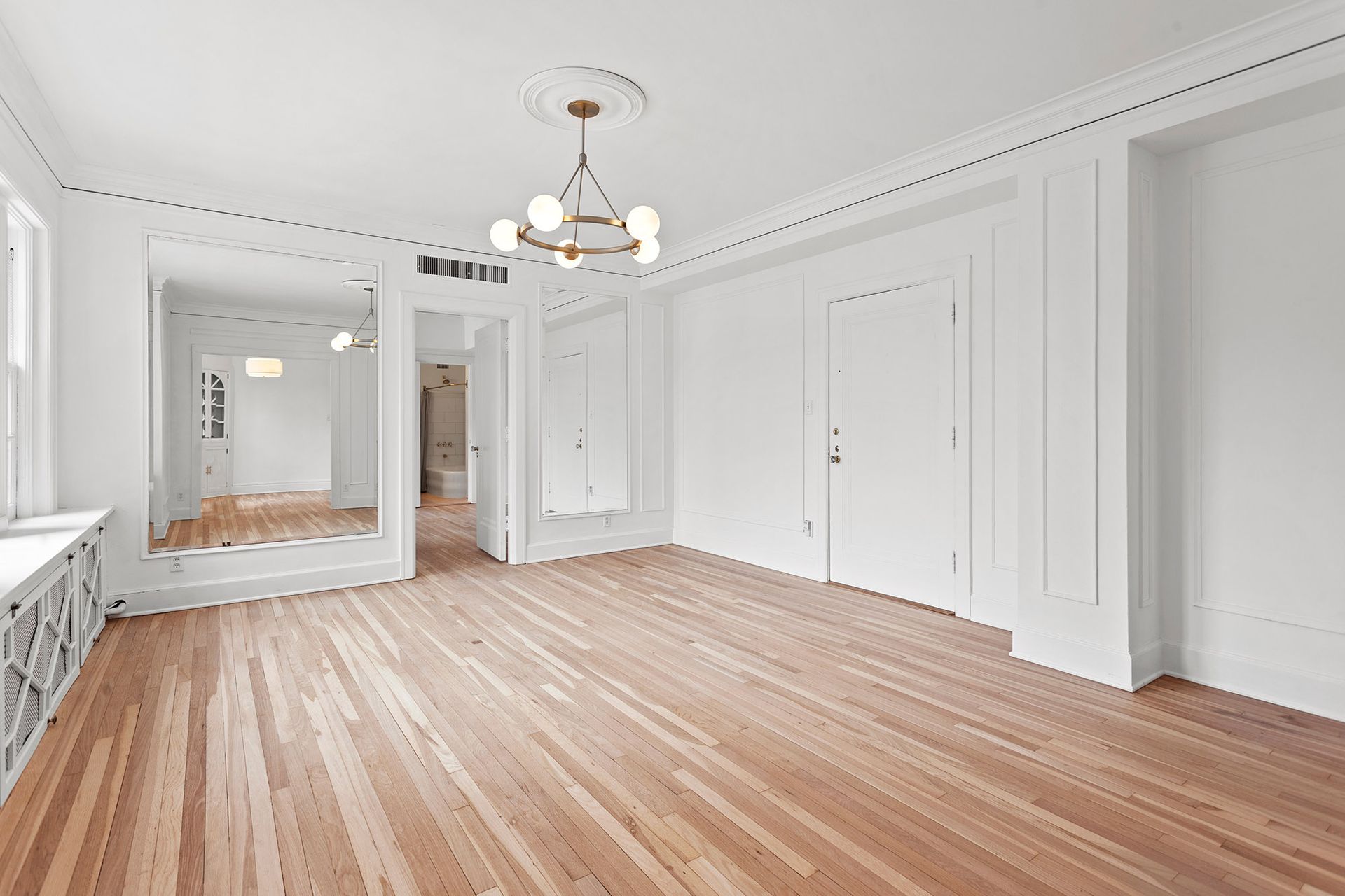 Empty room with wood floor, white walls and ceiling trim, and a chandelier.