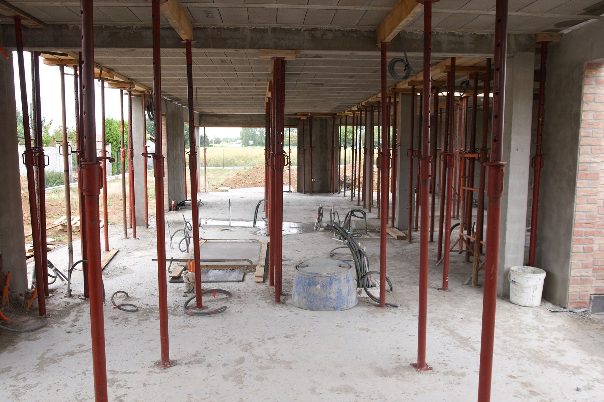 Interior of a building under construction, supported by red metal props. Concrete floor and ceiling visible.