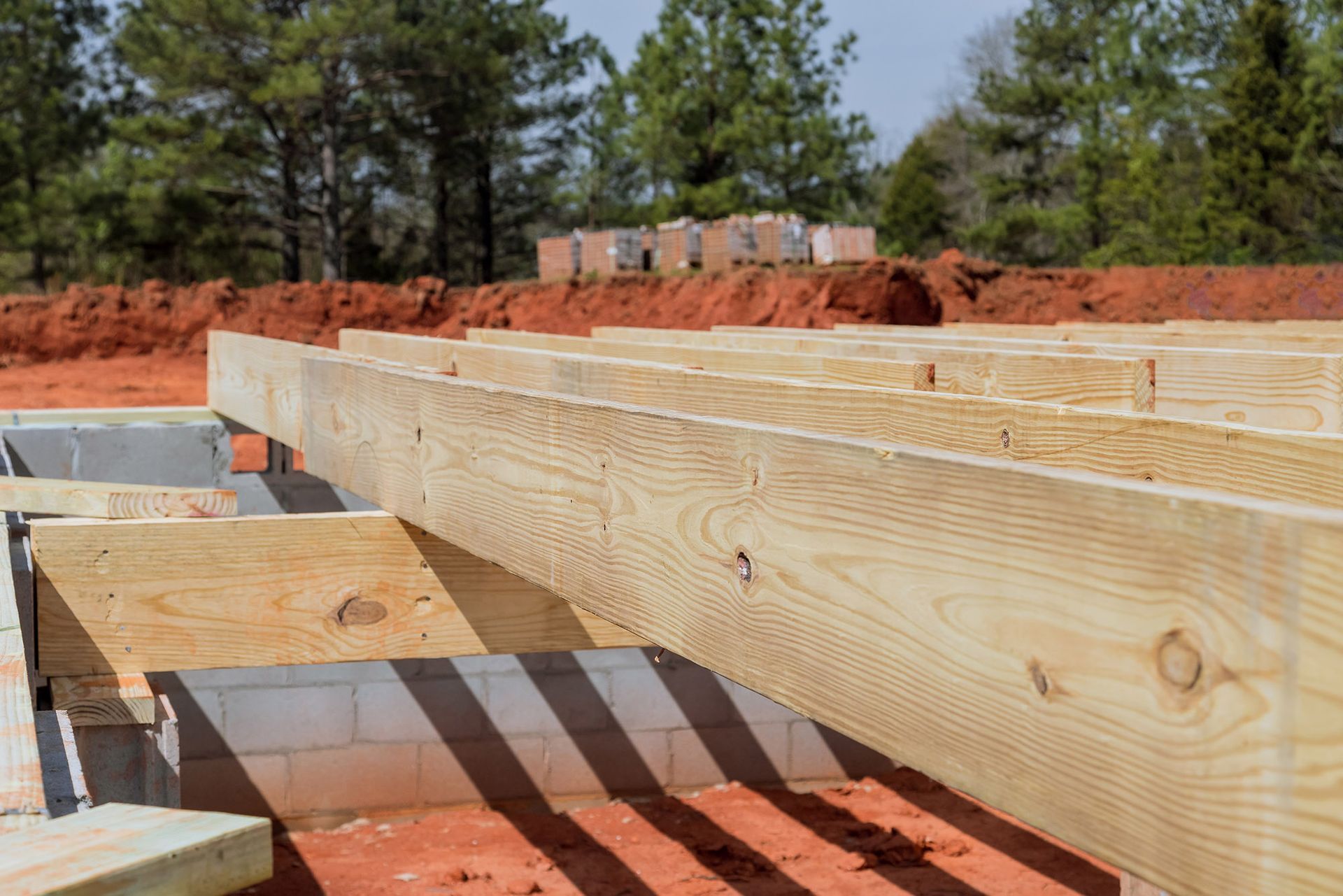 Wooden beams and cinder blocks forming the foundation of a new construction site, surrounded by red soil.