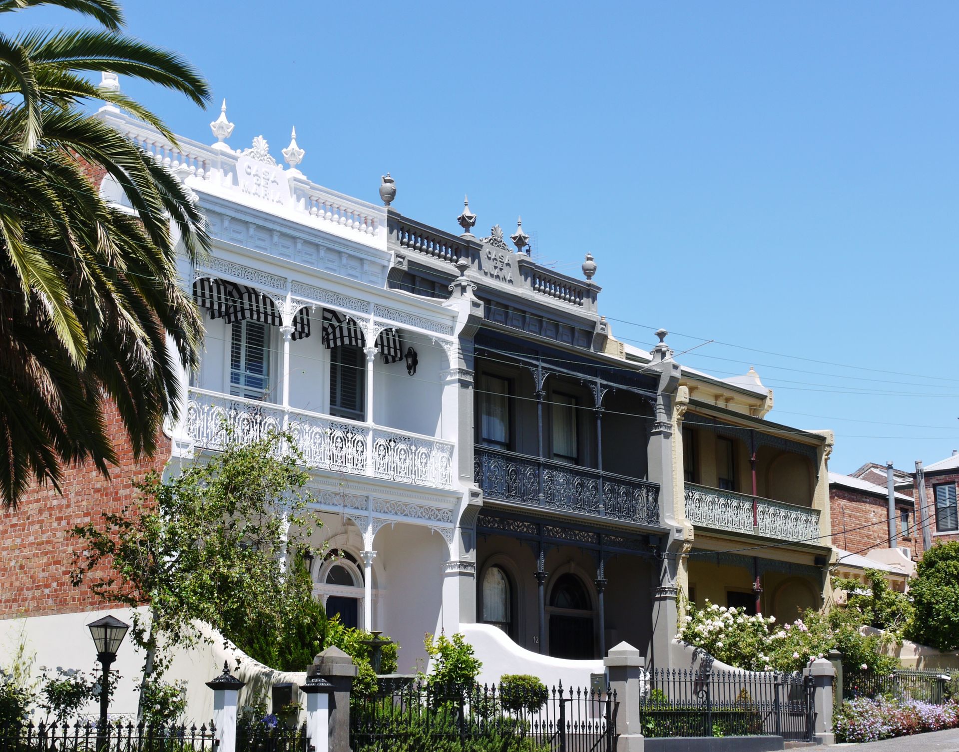Row of Victorian-style houses with decorative balconies in various colors against a blue sky.