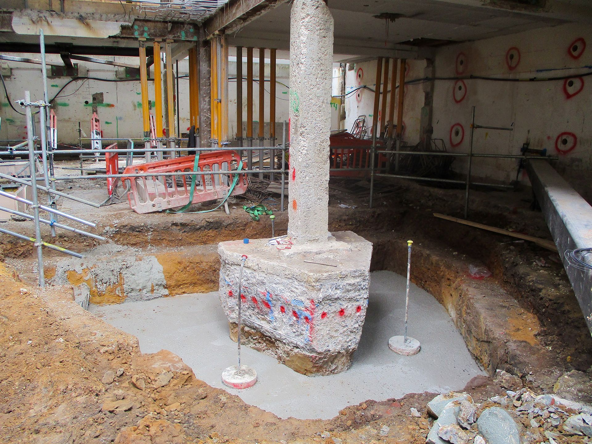 Construction site with concrete pillar, excavated earth, and support beams.