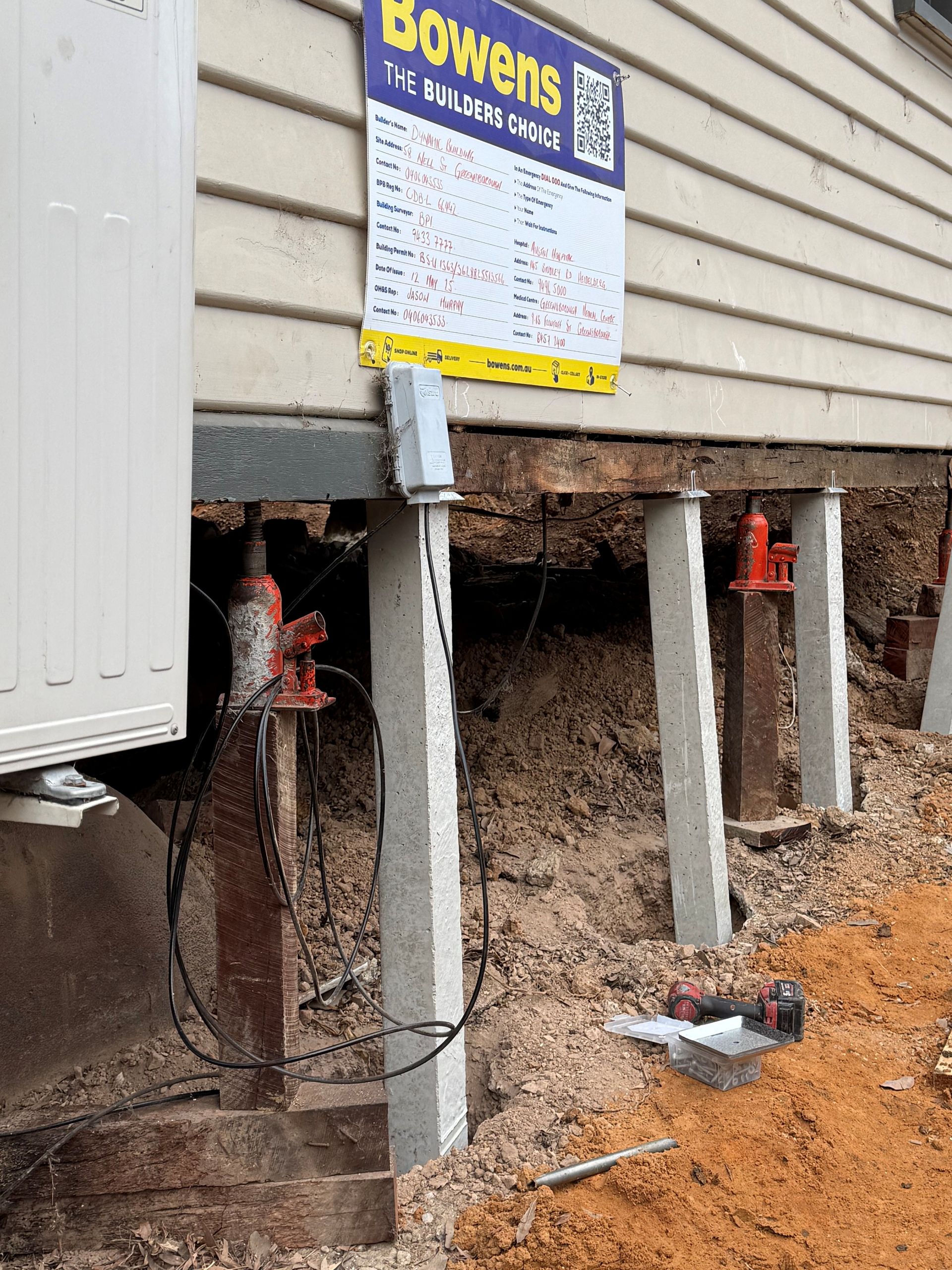Foundation repair: House supported by jacks and concrete piers. Soil exposed. Sign posted by company, "Bowens".