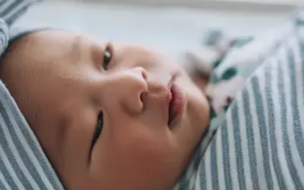 Asian baby wrapped in a striped blanket, eyes open, resting.