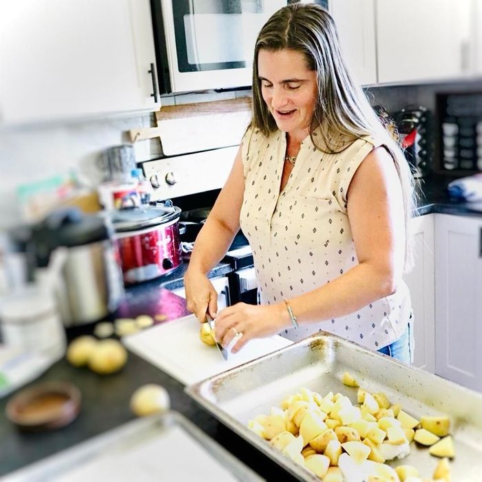 Woman in kitchen chopping potatoes, smiling. Chopped potatoes in a baking tray.