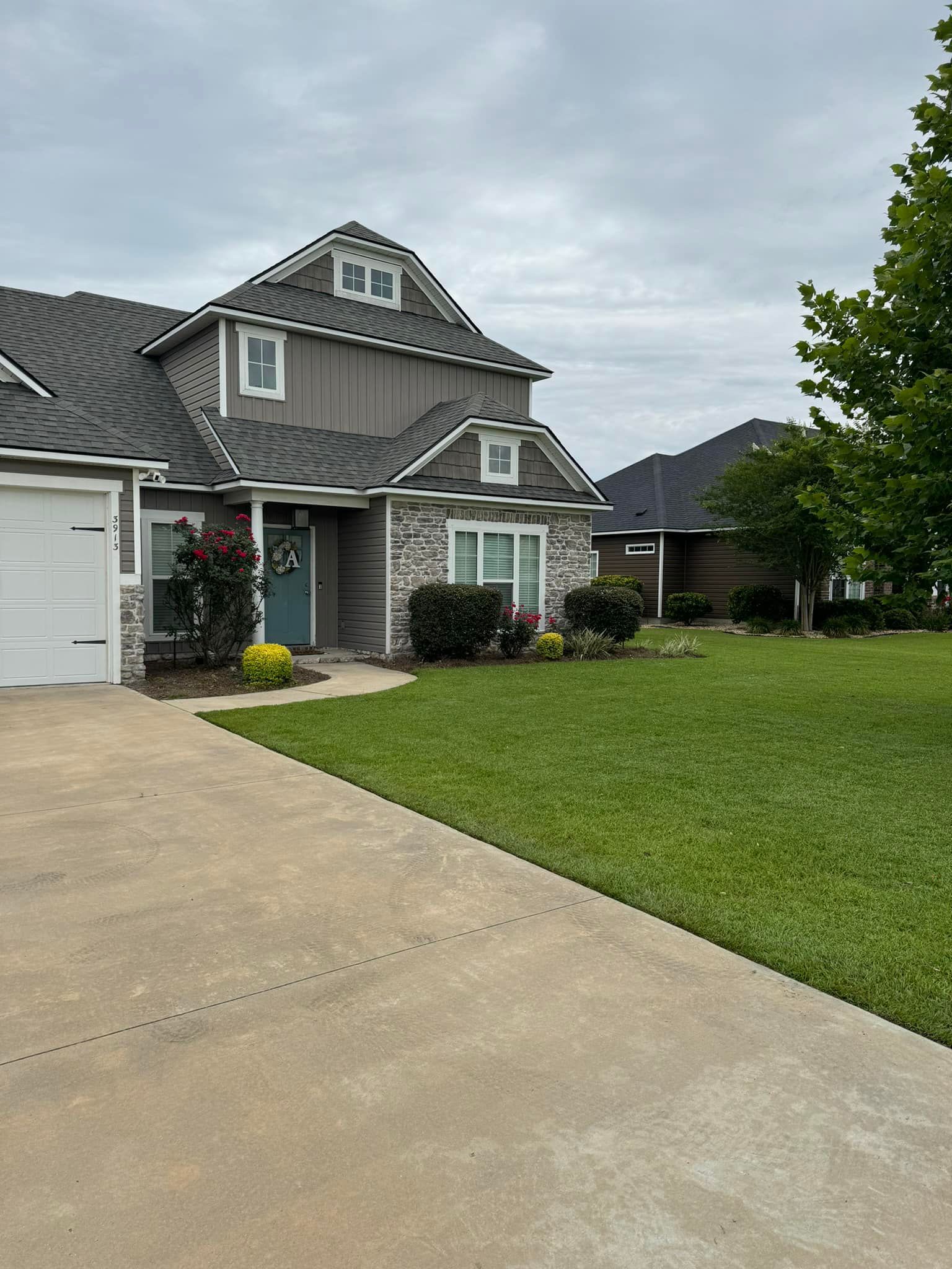 A large house with a gray roof and a white garage door is sitting on top of a lush green lawn.