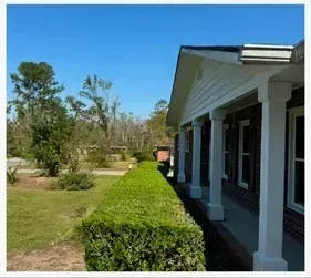 A house with a porch and a hedge in front of it