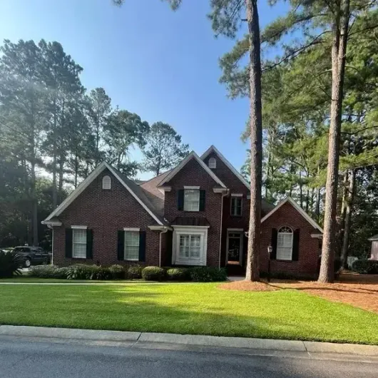 A large brick house with black shutters is surrounded by trees