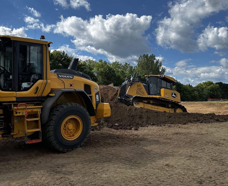 Yellow bulldozers grading dirt under a cloudy blue sky on a construction site