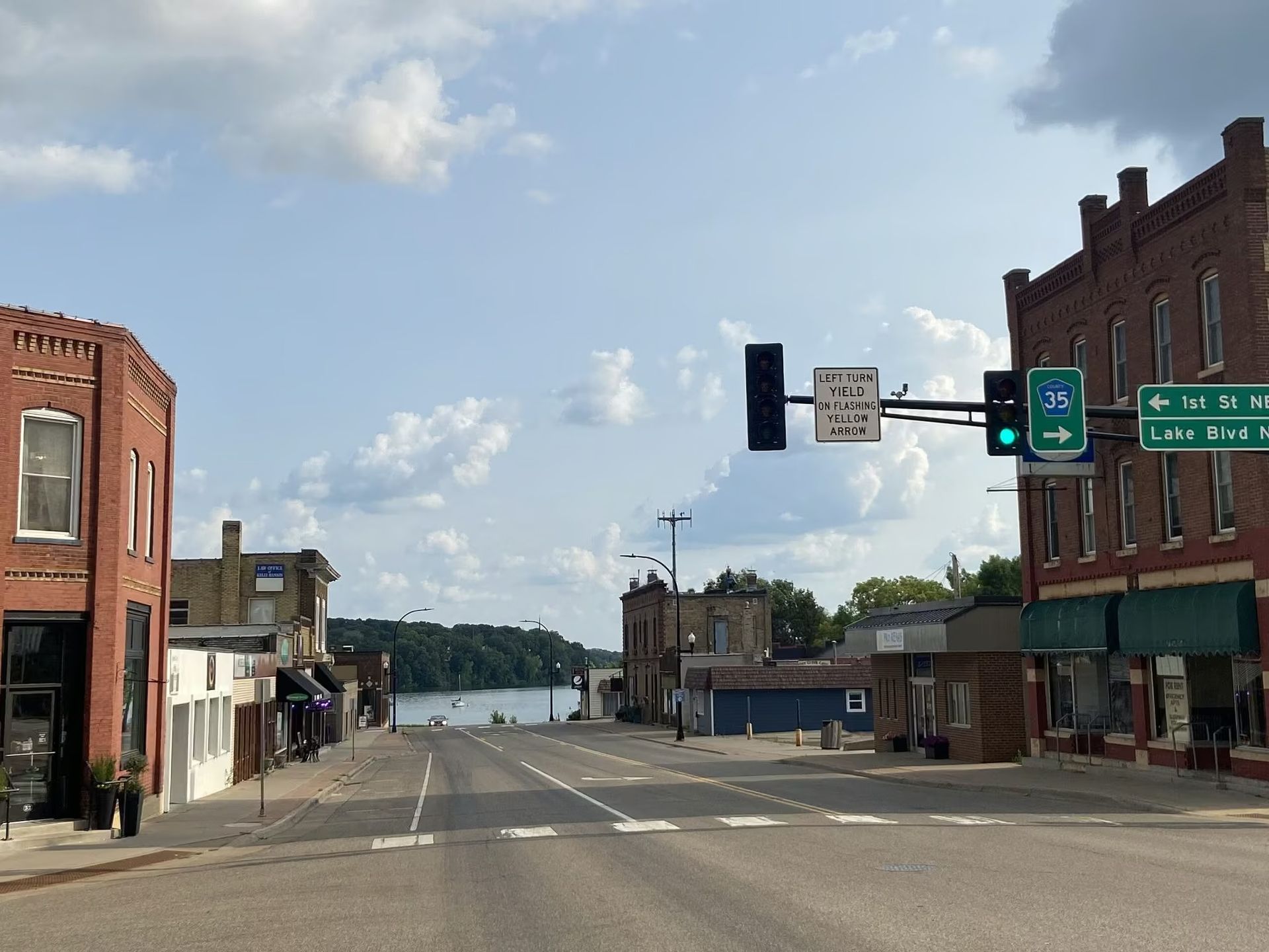 Small-town main street leading to a river, with empty road, brick buildings, and traffic lights.