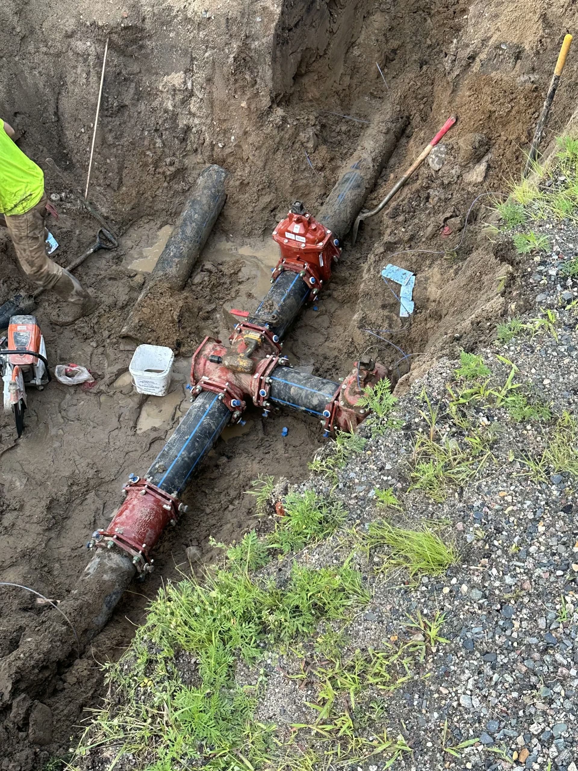 Excavated underground pipe junction with red valves and muddy trench walls