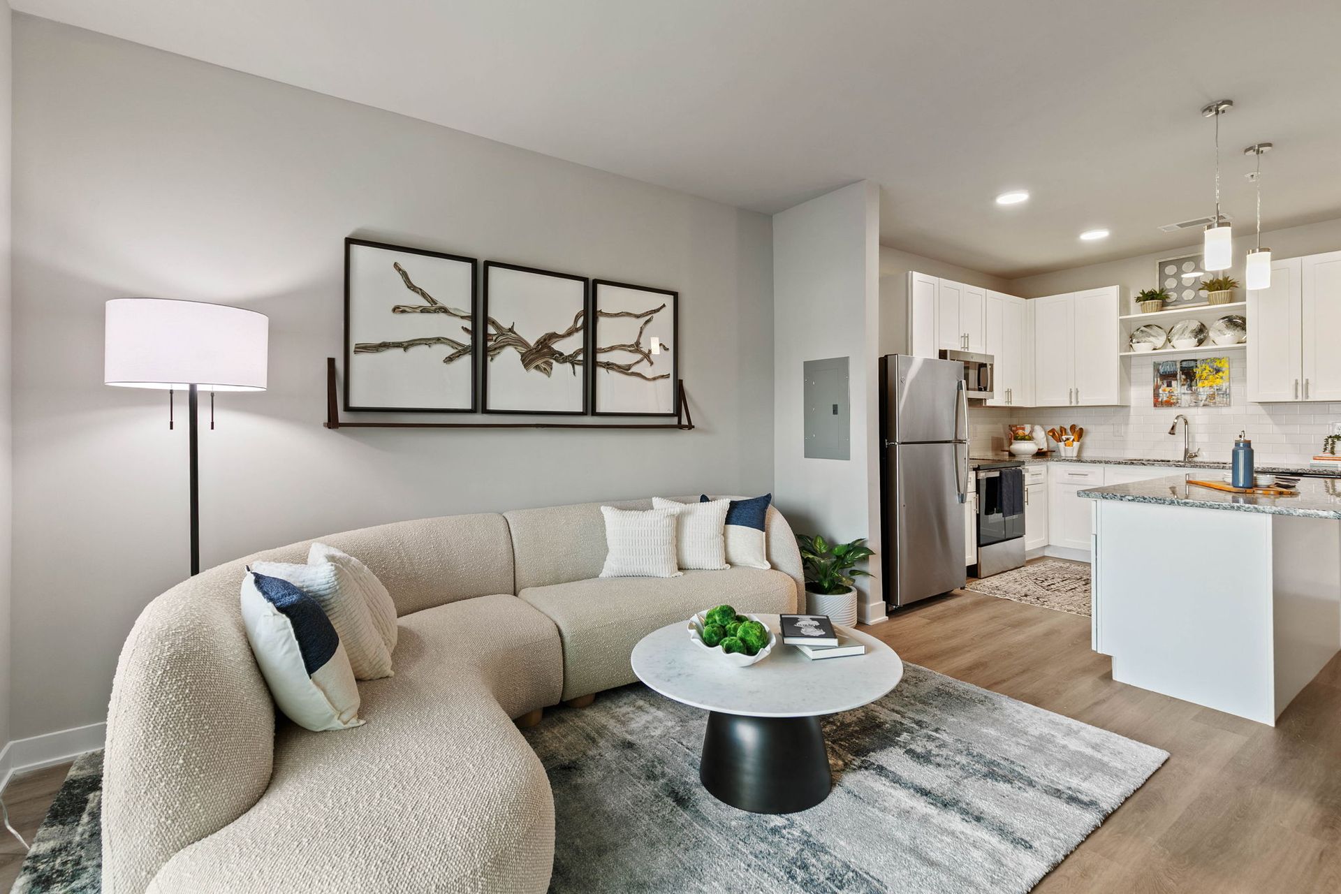 Living room with curved beige sofa, white kitchen, and round coffee table.