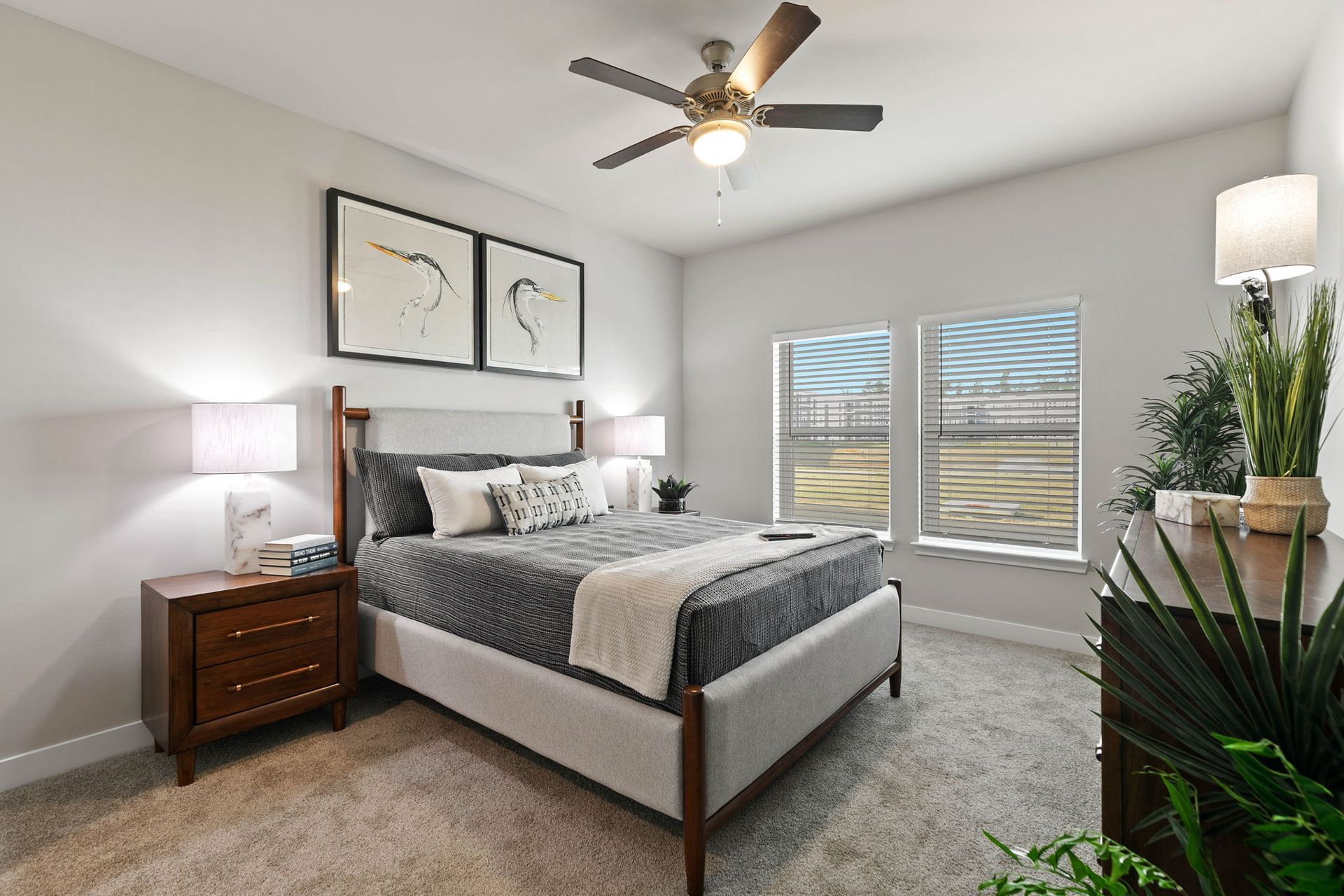 Bedroom with bed, nightstands, windows, art, and ceiling fan. Neutral colors, modern style.