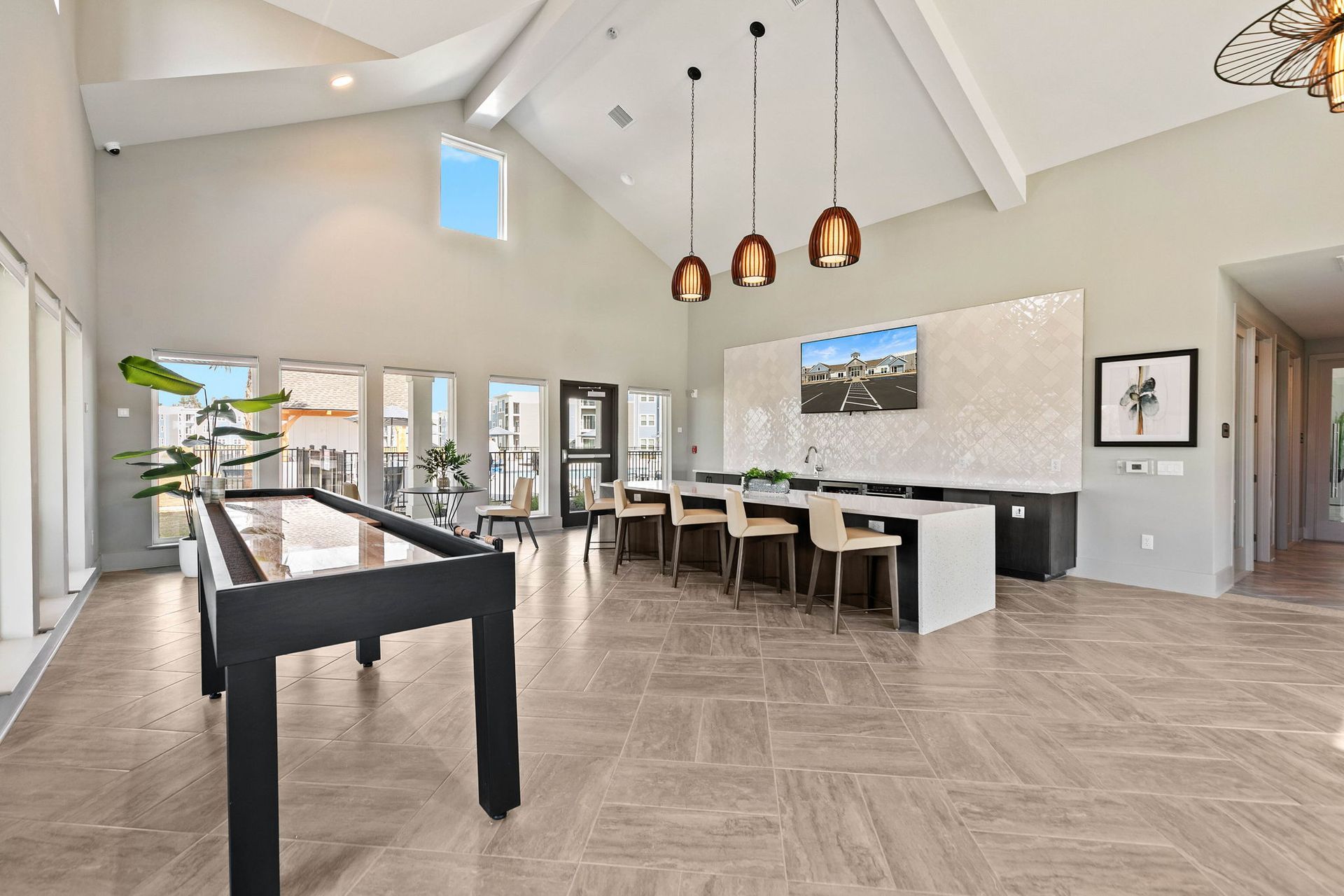 Spacious, light-filled room with large windows, a long table, bar stools, and decorative lighting.