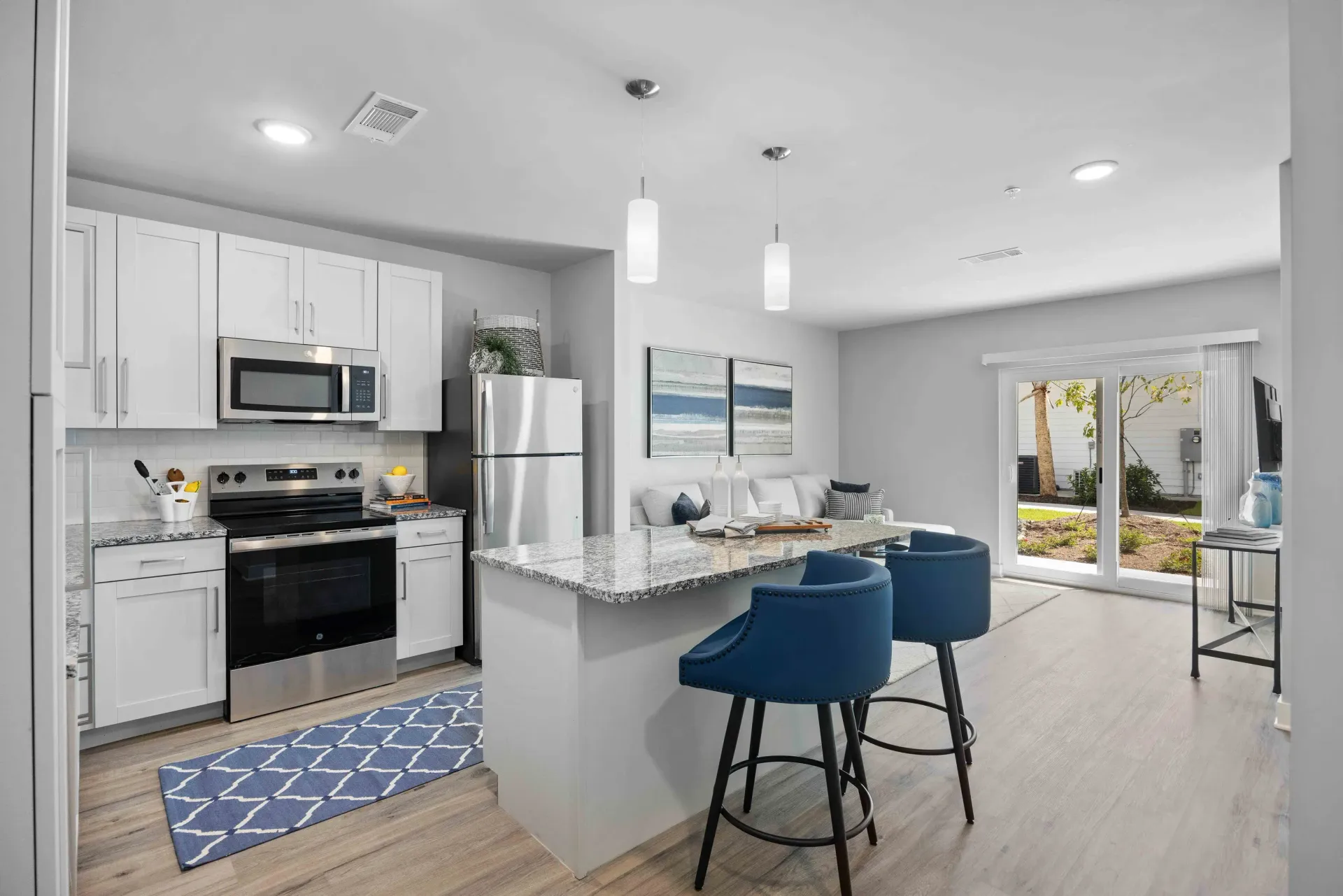 Modern kitchen with white cabinets, stainless steel appliances, and a gray countertop island with blue bar stools.