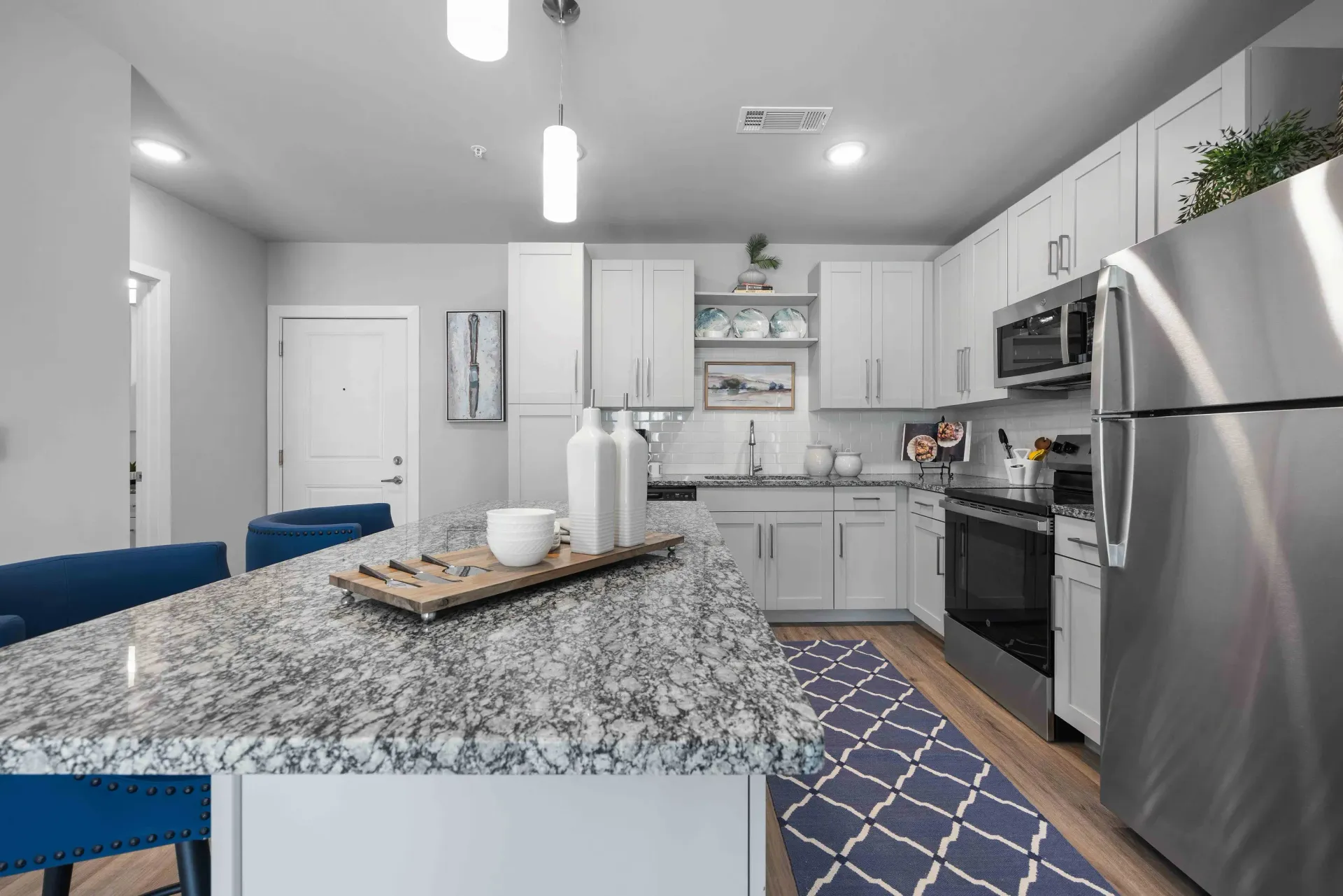 Modern kitchen with white cabinets, granite island, stainless steel appliances, and patterned rug.