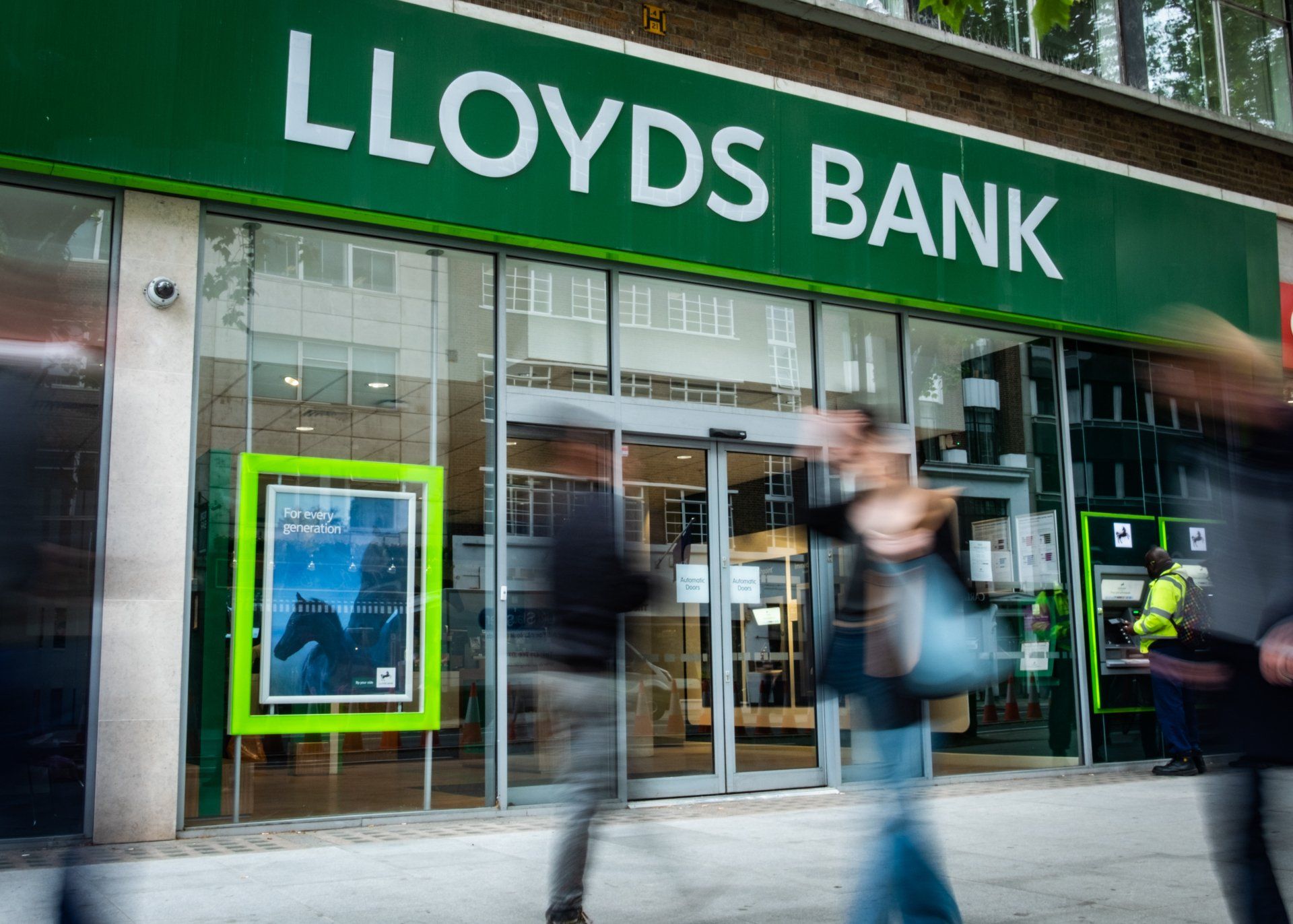 Picture of the front of a Lloyd's bank branch with blurred ppl outside