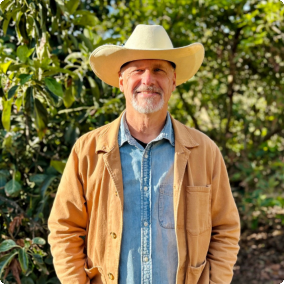 Innovation hub team lead smiles outdoors in front of leafy trees.