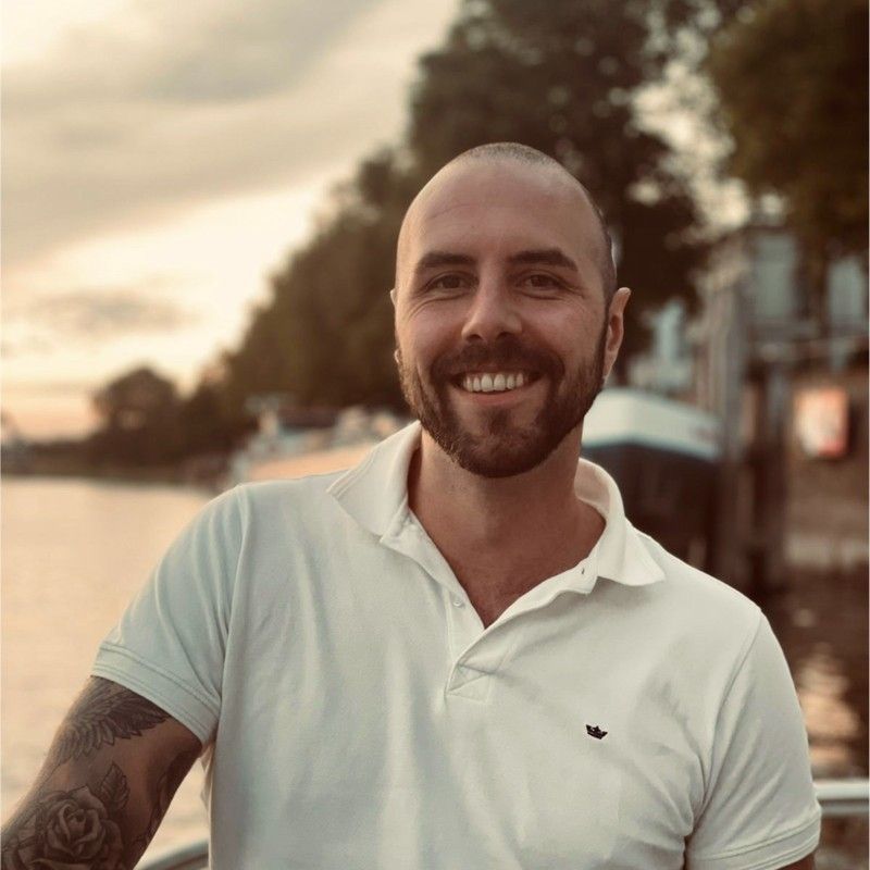 Een kale man met een baard die een wit poloshirt draagt