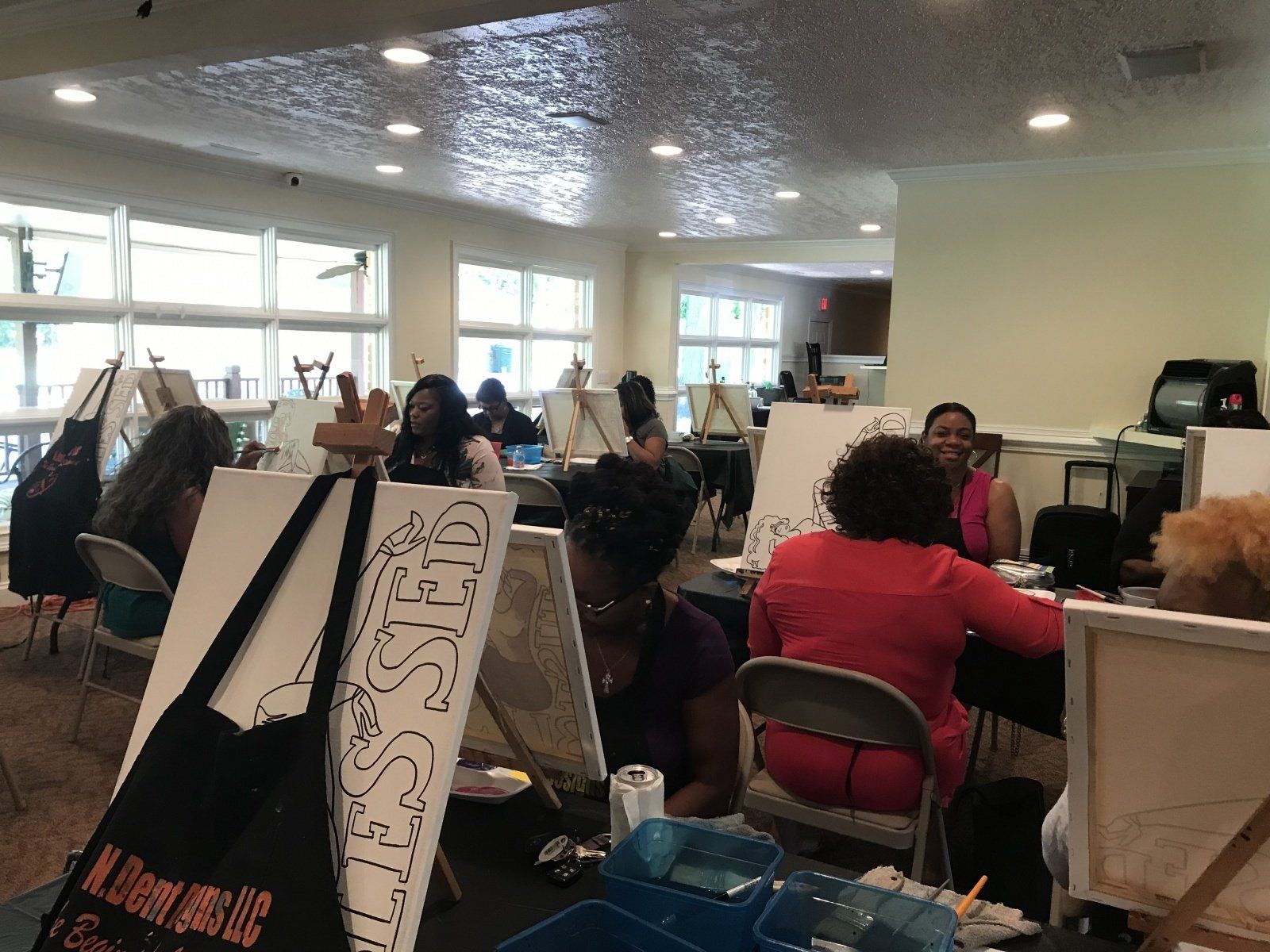 A group of people are sitting at tables painting on canvases.