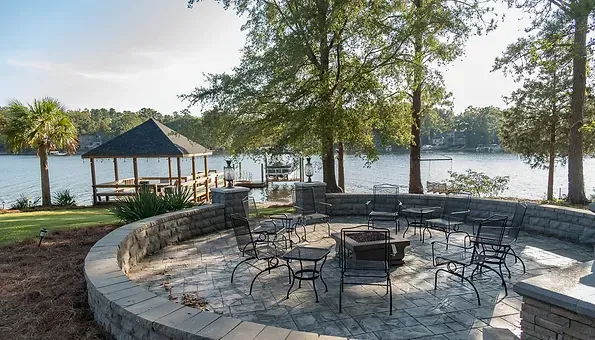 There is a fire pit in the middle of a patio next to a lake.