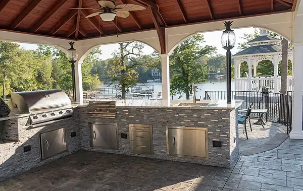 A large outdoor kitchen under a gazebo with a view of a lake.