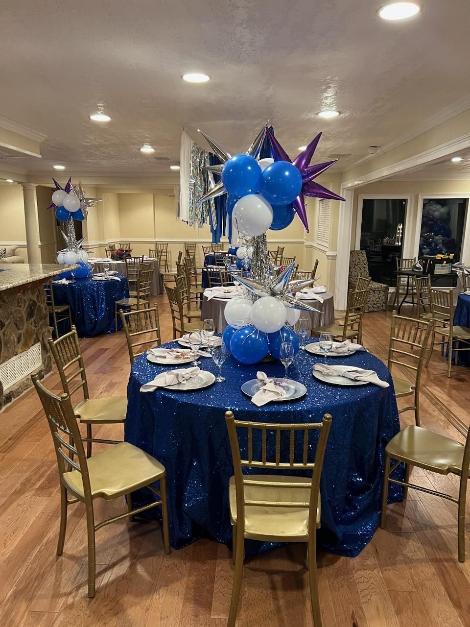 A room filled with tables and chairs decorated with blue and white balloons.