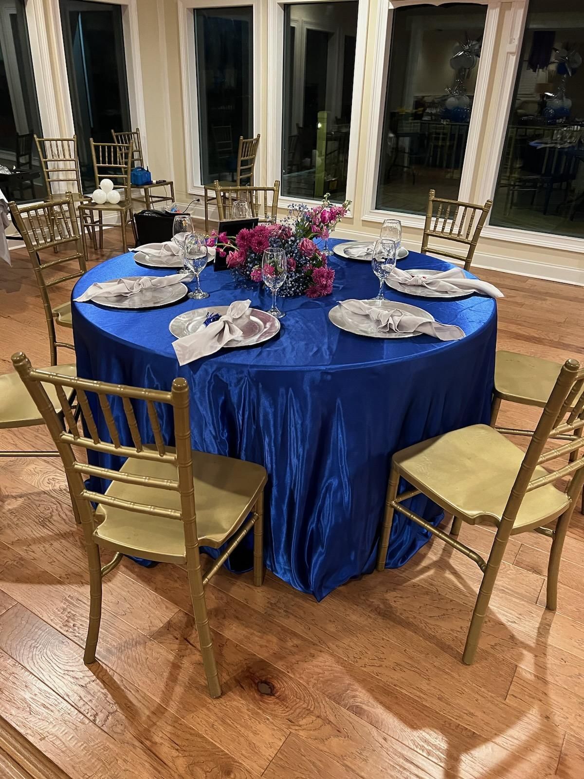 A round table with a blue tablecloth and gold chairs in a room.