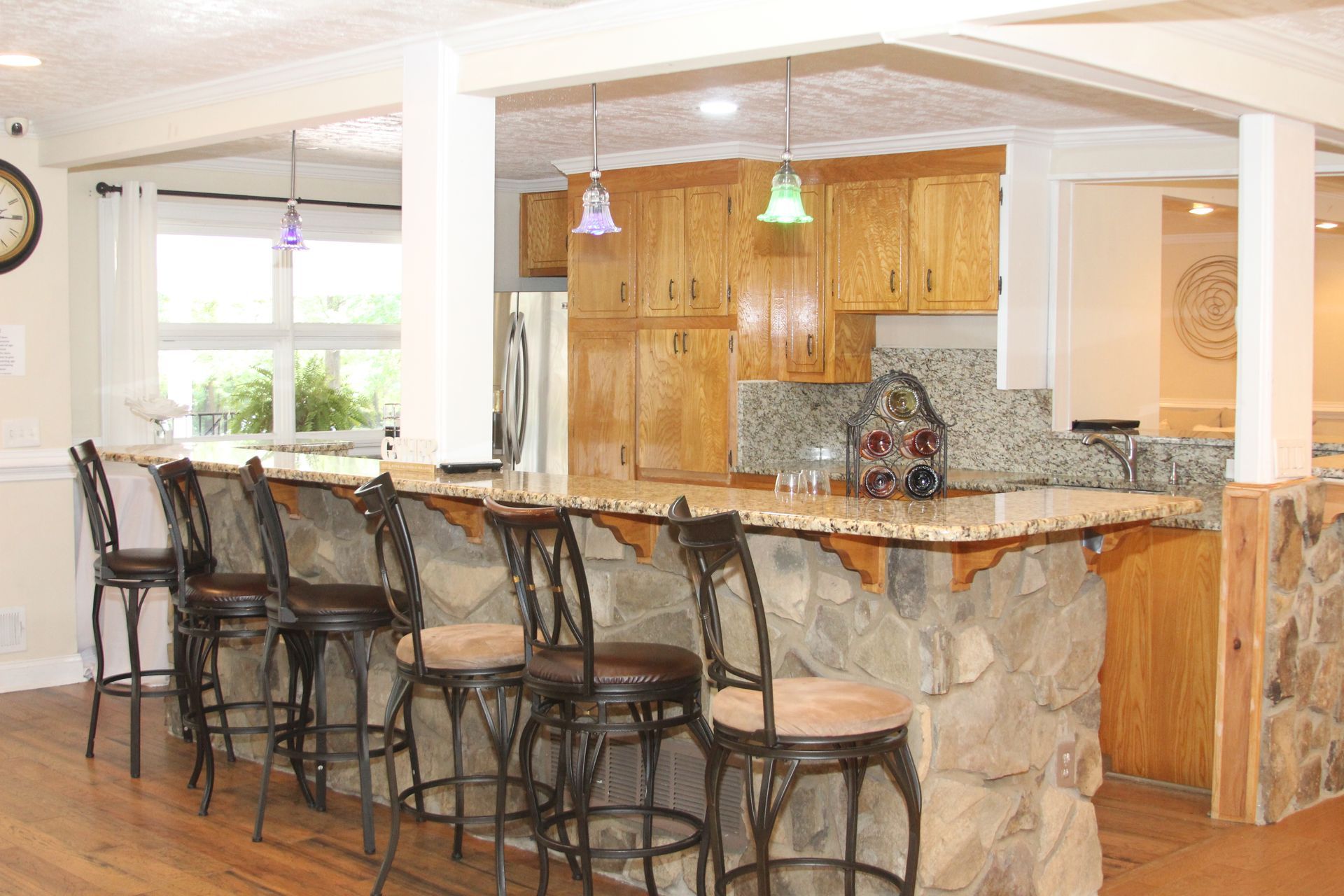 A kitchen with a stone bar and stools and a clock on the wall.
