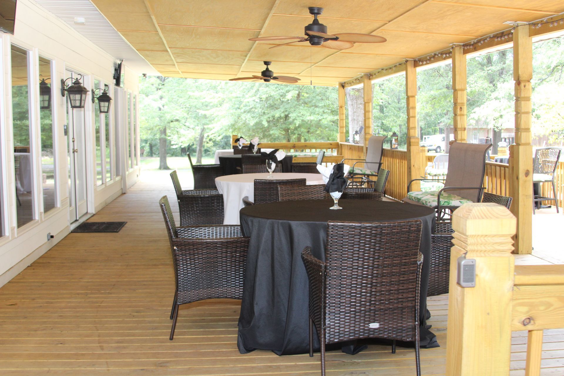 A wooden porch with tables and chairs and a ceiling fan