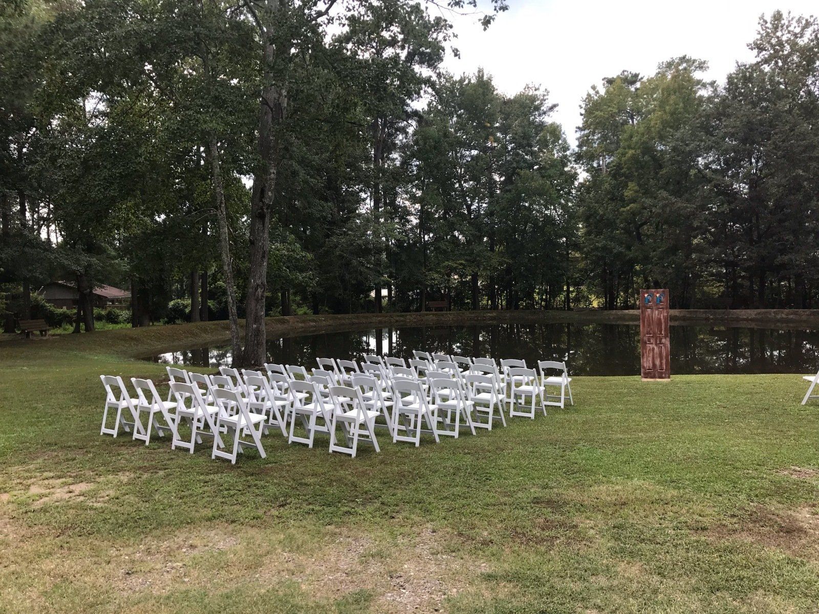 A row of white folding chairs are lined up in a circle in a grassy field.