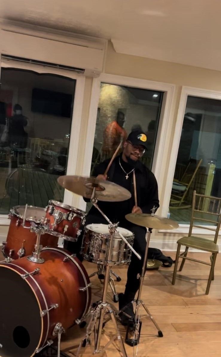 A man is playing drums in a room in front of a window.