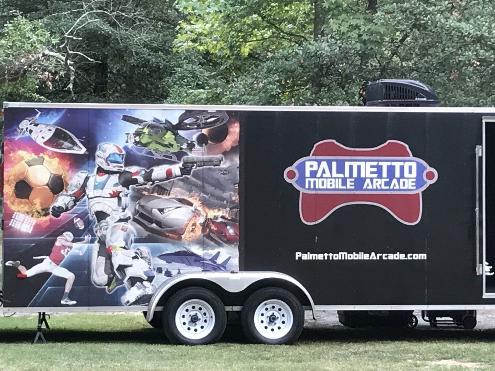 A palmetto mobile arcade trailer is parked in a grassy field.