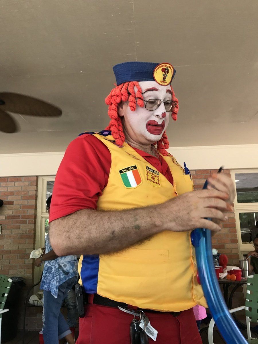 A man dressed as a clown is holding a blue balloon