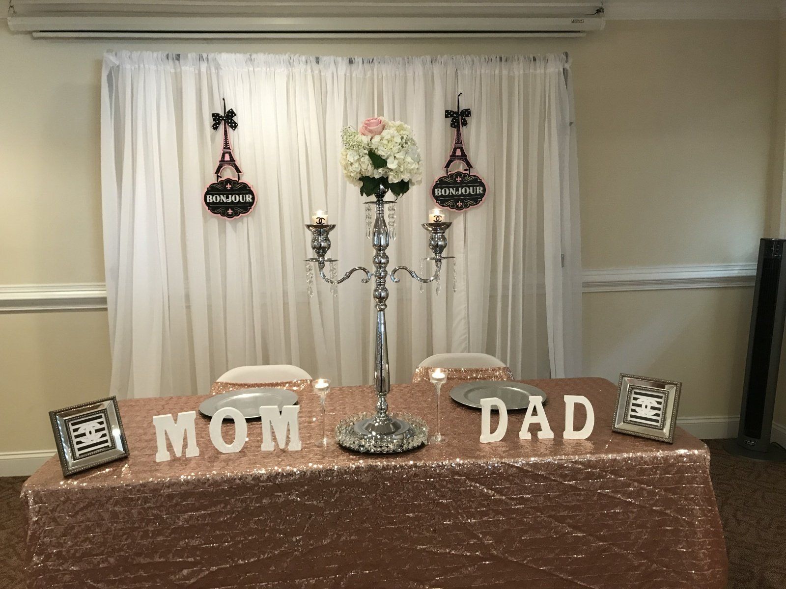 A table with a rose gold tablecloth and a candle holder with the words mom and dad on it.